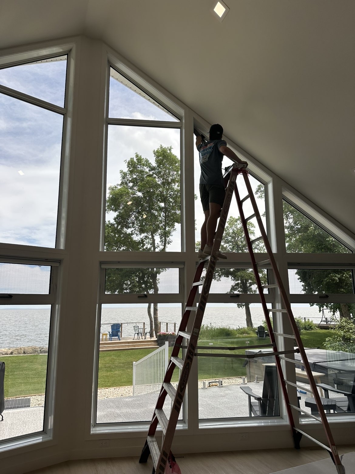 Newmar worker cleaning interior windows from a ladder inside a home
